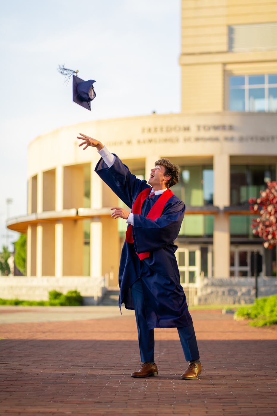 Graduate tossing his cap in front of a campus building